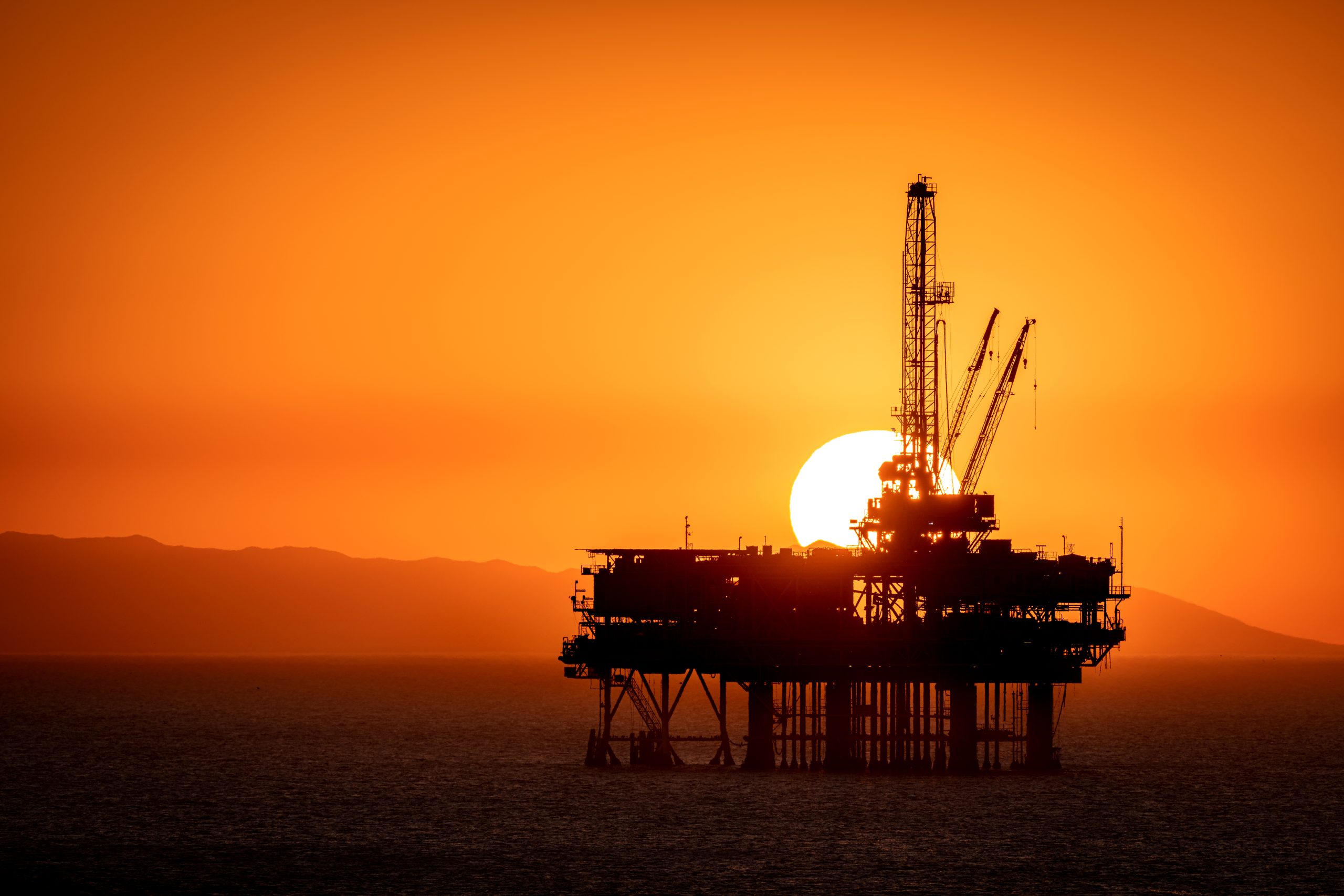 Offshore oil platform off the coast of California frames against an orange sky full of smoke from a nearby fire as the sun sets behind the rig.